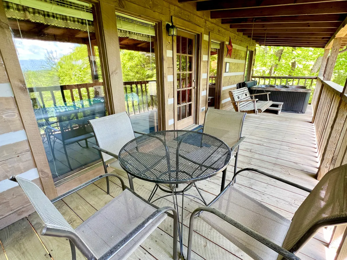 An outdoor dining table and chairs sit on a spacious deck overlooking trees, perfect for shared meals, sunset views, or soaking in the peaceful mountain air. The setting invites intimate picnics or quiet moments together.