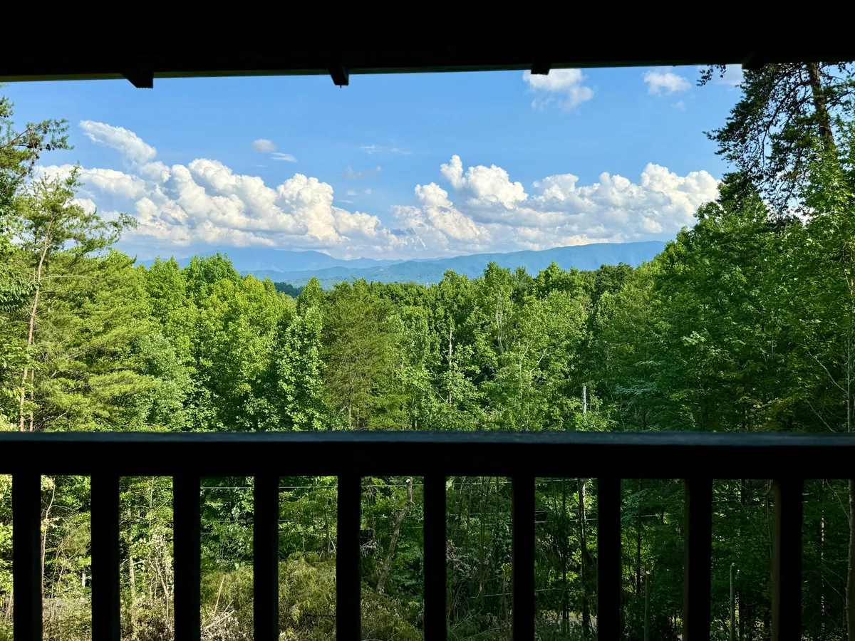 This image offers a panoramic view of lush green trees, distant Smoky Mountain peaks, and a blue sky dotted with clouds. The scene embodies the tranquility and natural beauty that draws couples to the area for scenic drives and romantic getaways.