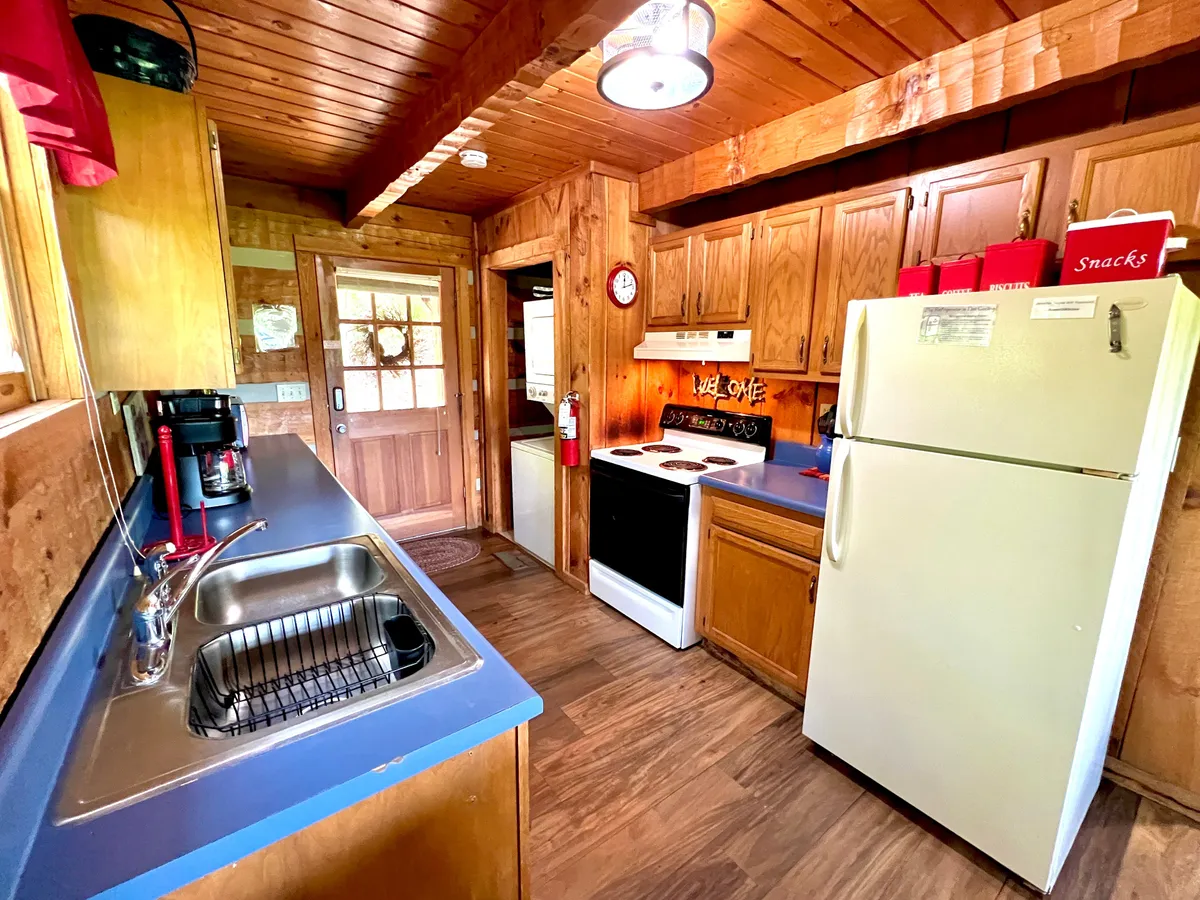 A functional kitchen view featuring the kitchen sink, stove, and refrigerator, with a view into an adjacent room through a doorway. The space is clearly set up for meal preparation and family gatherings, reinforcing the idea of culinary creativity and convenience.
