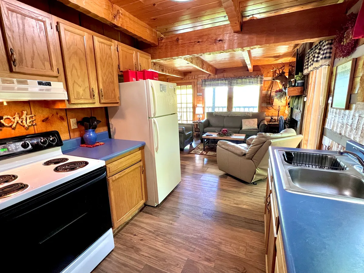 A warm, inviting kitchen space showcasing wooden cabinetry, modern kitchen appliances, and a view that extends into the living area. The countertop is clear and ready for meal prep, and the setup hints at a cozy, communal vibe, ideal for cooking and conversation.